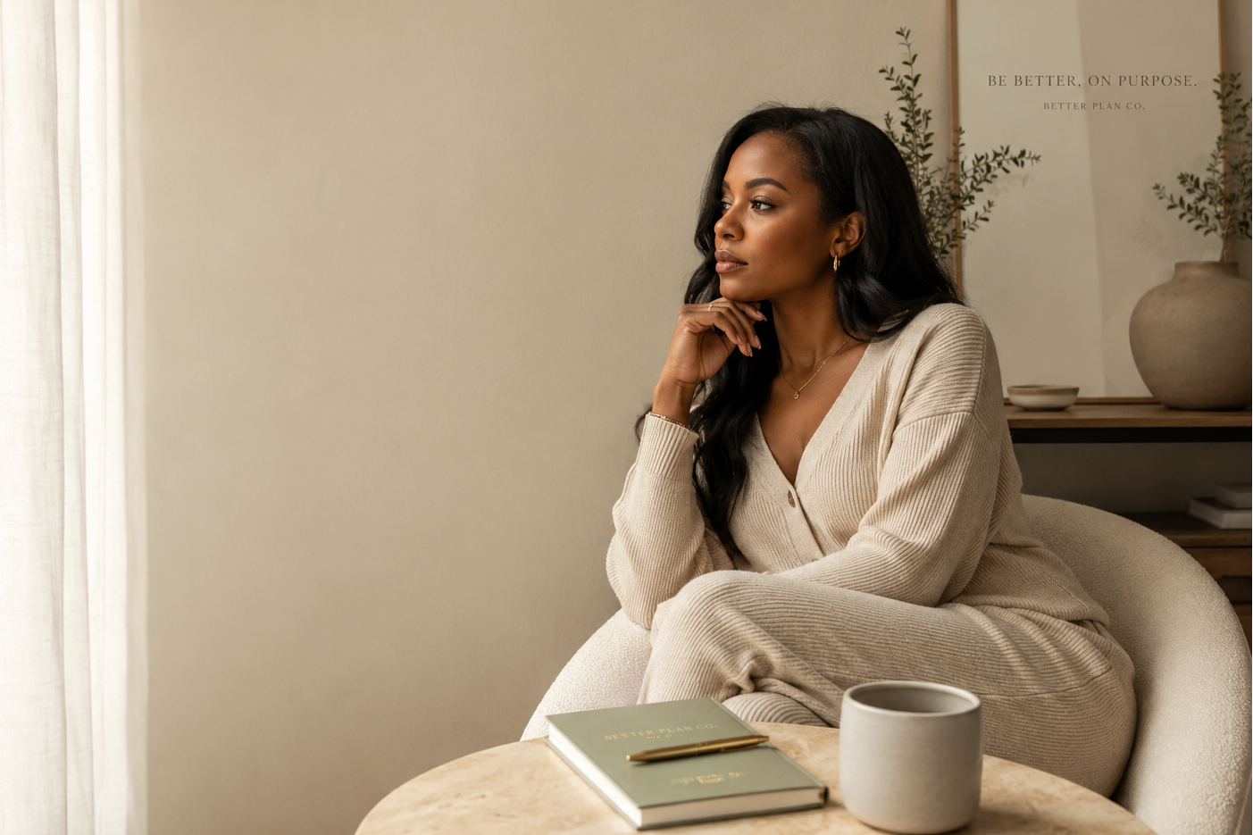 Black woman sitting thoughtfully by a window with a notebook and coffee during a quiet moment of reflection.