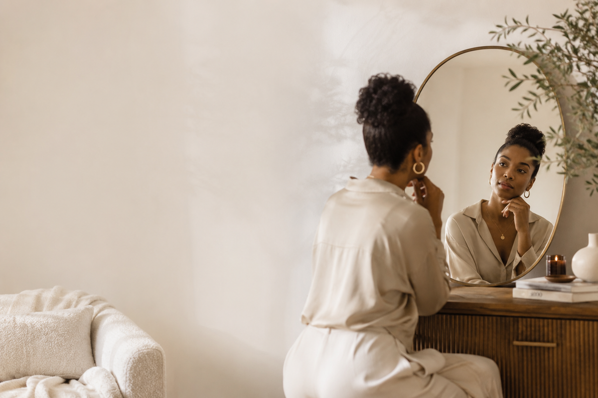 Black woman looking at herself in a mirror during a quiet moment of self reflection and personal clarity.